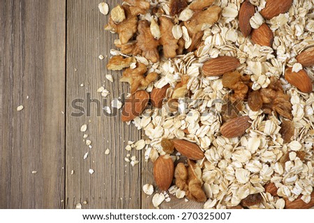 Pile of dry oatmeal flakes with walnuts, almonds and raisins on rustic wooden background. Top view point.