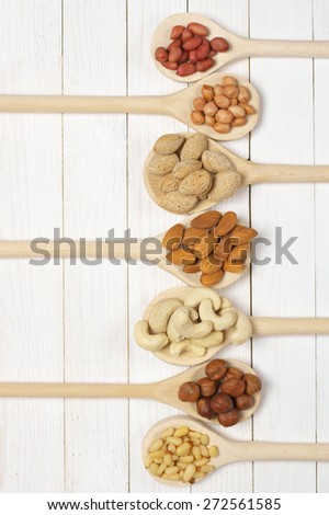 Variety of assorted nuts in spoons on white wood background with copy space. Top view point.