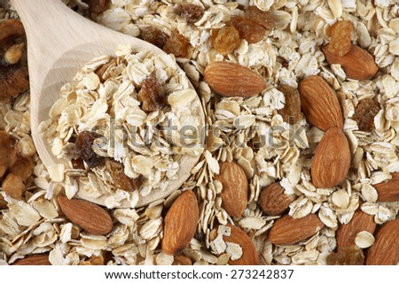 Pile of dry oatmeal flakes with walnuts, almonds, raisins and wooden spoon close-up. Top view point.