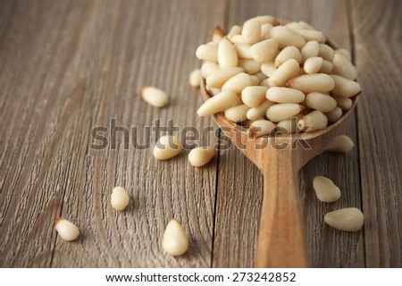 Peeled pine nuts in wooden spoon on wood background.