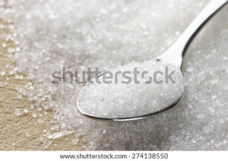 Close-up of granulated sugar in spoon and sugar pile. Shallow DOF.
