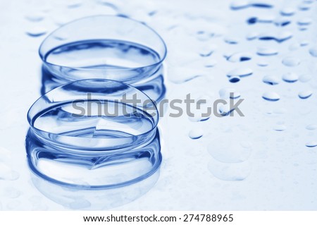 Close-up of two wet soft contact lenses with reflection on light background with drops and copy space. Shallow DOF.