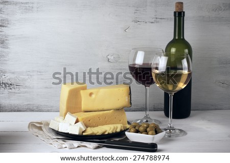 Red and white wine in glasses and bottle and assorted cheese with olives on rustic wooden background.