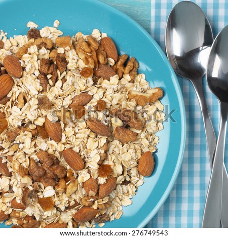 Dry oatmeal flakes with walnuts, almonds and raisins in aquamarine plate with spoons and napkin. Top view point.