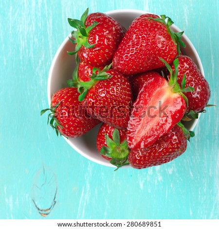 Fresh strawberries in bowl on aquamarine painted rustic wooden background. Top view point.