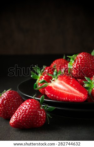 Fresh strawberries in black plate on dark wooden background.