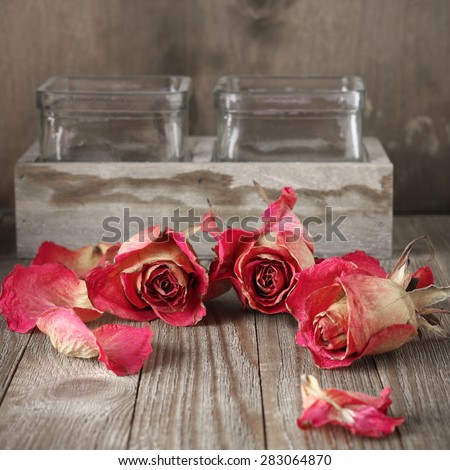 Dried pink roses heads and petals on rustic wooden table near wood box with glass jars. Shallow DOF.