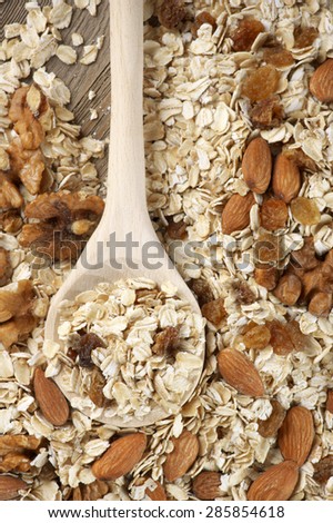 Pile of dry oatmeal flakes with walnuts, almonds, raisins and wooden spoon. Top view point.