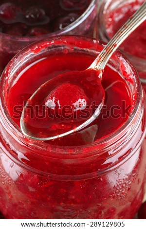 Assorted jams in glass jars and strawberry jam in spoon close-up..