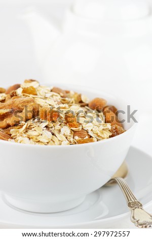 Dry oatmeal flakes with walnuts, almonds and raisins in white bowl against white dishware. High key. Shallow DOF.