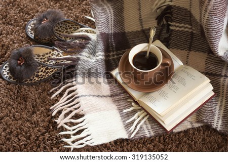 Woolen plaid, coffee cup, book and slippers on shaggy carpet. Top view. Text in book unreadable.