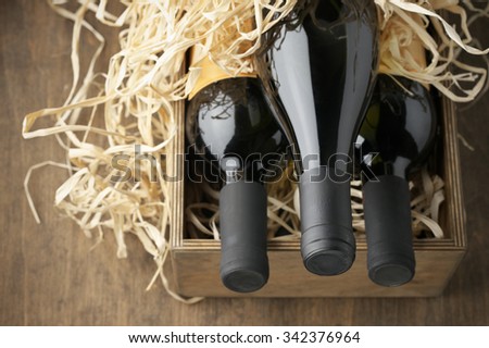 Three closed wine bottles lying on straw in vintage wooden box on wood background.