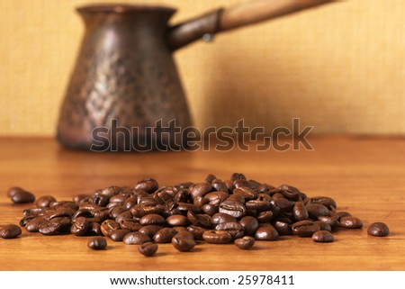 Coffee beans and vintage cezve on brown wood surface. Selective focus on beans.
