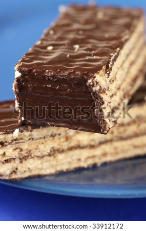 Stack of chocolate wafers close-up on blue plate. Selective focus at foreground of upper piece.
