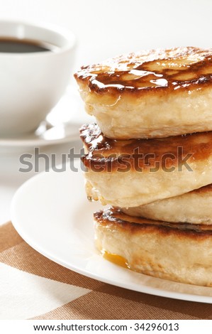 Stack of thick pancakes with honey on white plate and white cup of coffee.