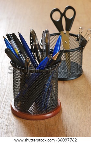 Pens, pencils and scissors in black metal containers on wooden desk.