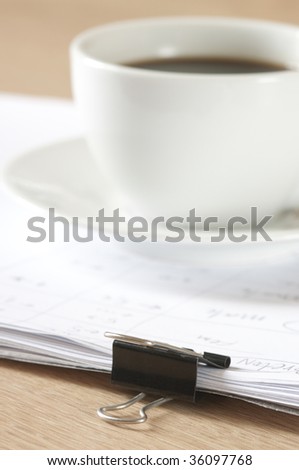 Pile of paper with metal clamp and cup of coffee.