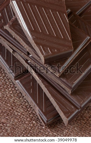 Stack of broken dark chocolate bar on brown canvas.