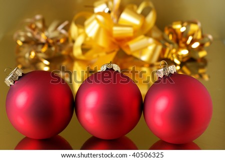 Red Christmas tree decorations against gold ribbon on golden background.