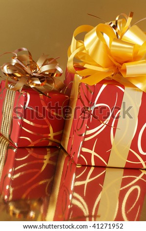 Two red and gold gifts on gold background with reflection.