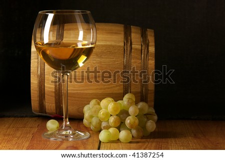 Glass of white wine, white grape and souvenir barrel on wooden surface.