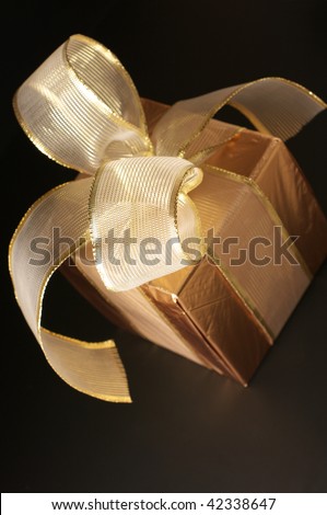 Gold foil gift with gold translucent bow on black background.