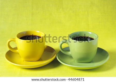 Black coffee in yellow and green cups with saucers on lemon yellow linen cloth.