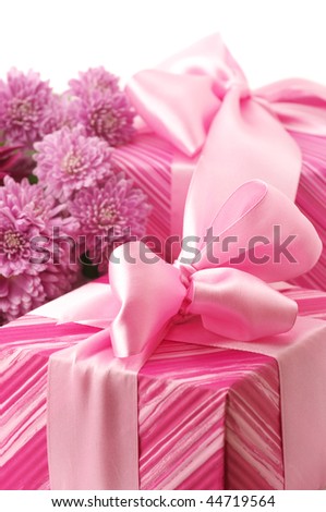 Close-up of two pink gifts with satin bows and bouquet of chrysanthemums on white background.