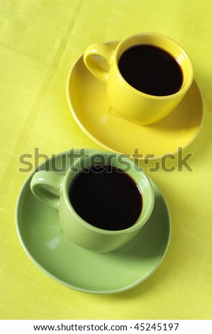 Black coffee in yellow and green cups with saucers on lemon yellow linen cloth.