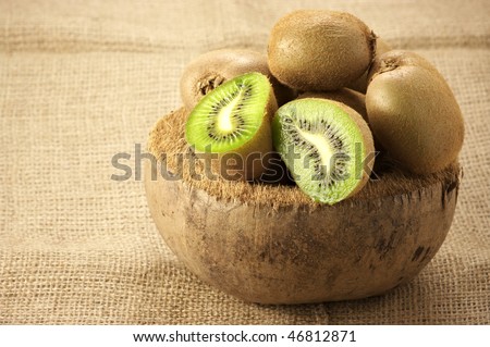 Heap of whole and cut kiwi in coconut bowl.