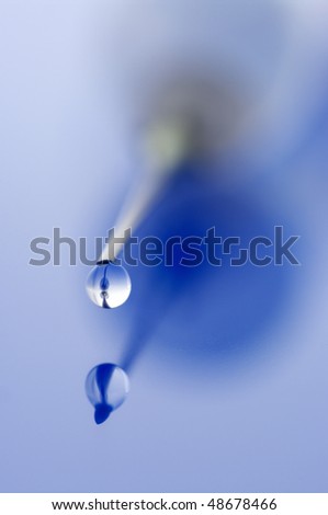 Close-up of syringe with drop on blue background. Selective focus on needle point and drop.