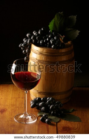 Glass of red wine, dark grape and souvenir barrel on wooden surface.