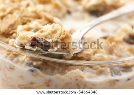 Close-up of muesli in spoon on glass bowl of muesli with milk.