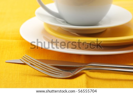 Yellow and white plates and cup, stainless fork and knife on yellow linen tablecloth.