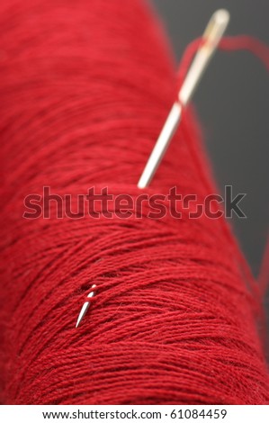 Close-up of needle with red thread in red reel on dark gray background.
