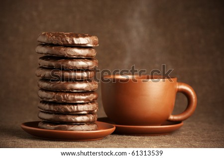 Stack of chocolate cookies and cup of coffee on brown canvas.