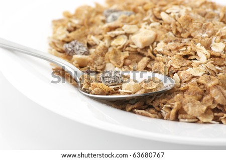 Heap of muesli in white plate with spoon on white background.
