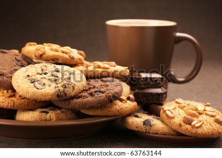 Assorted cookies in brown plate and brown mug of coffee on brown canvas.