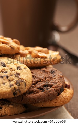 Assorted cookies in brown plate and brown mug of coffee on brown canvas.