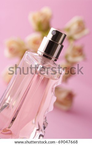 Bottle of opened pink perfume with roses on pink background.