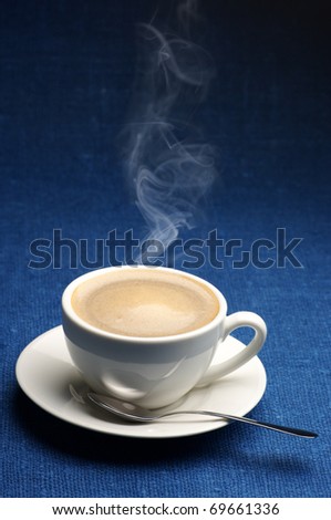 White cup of hot coffee with steam on dark blue canvas.