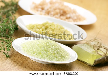 Close-up of various bath salt in white plates and handmade soap on wooden surface.