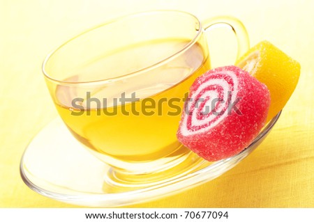 Red and yellow candy and glass cup of green tea on yellow background.