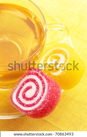 Red and yellow candy and glass cup of green tea close-up on yellow background.