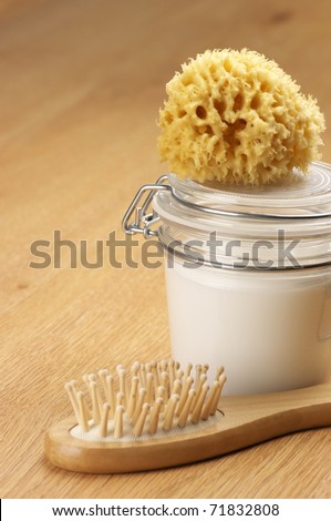 Jar of cosmetic cream, bath sponge and hair brush on wooden surface.