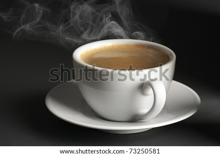 White cup of hot coffee with steam on dark gray background.