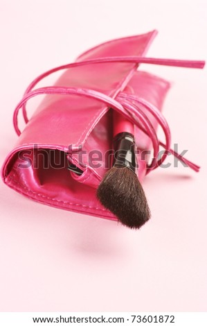 Pink cosmetic bag with make-up brush on light pink background.