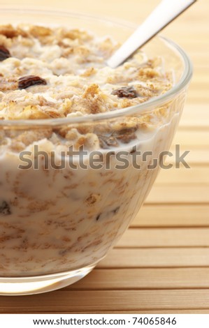Close-up of muesli with milk in glass bowl and spoon on wooden surface.