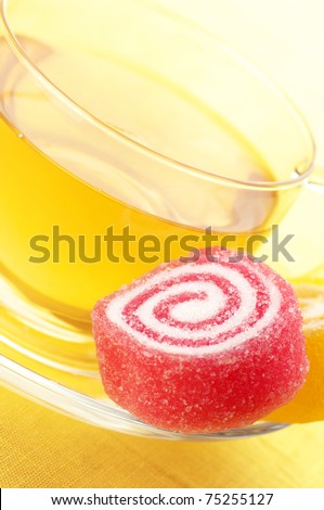 Red and yellow candy and glass cup of green tea close-up on yellow background.