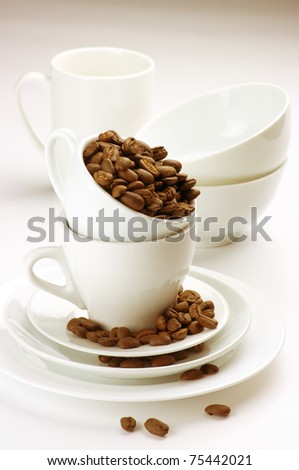 White tableware with roasted coffee beans on light background.